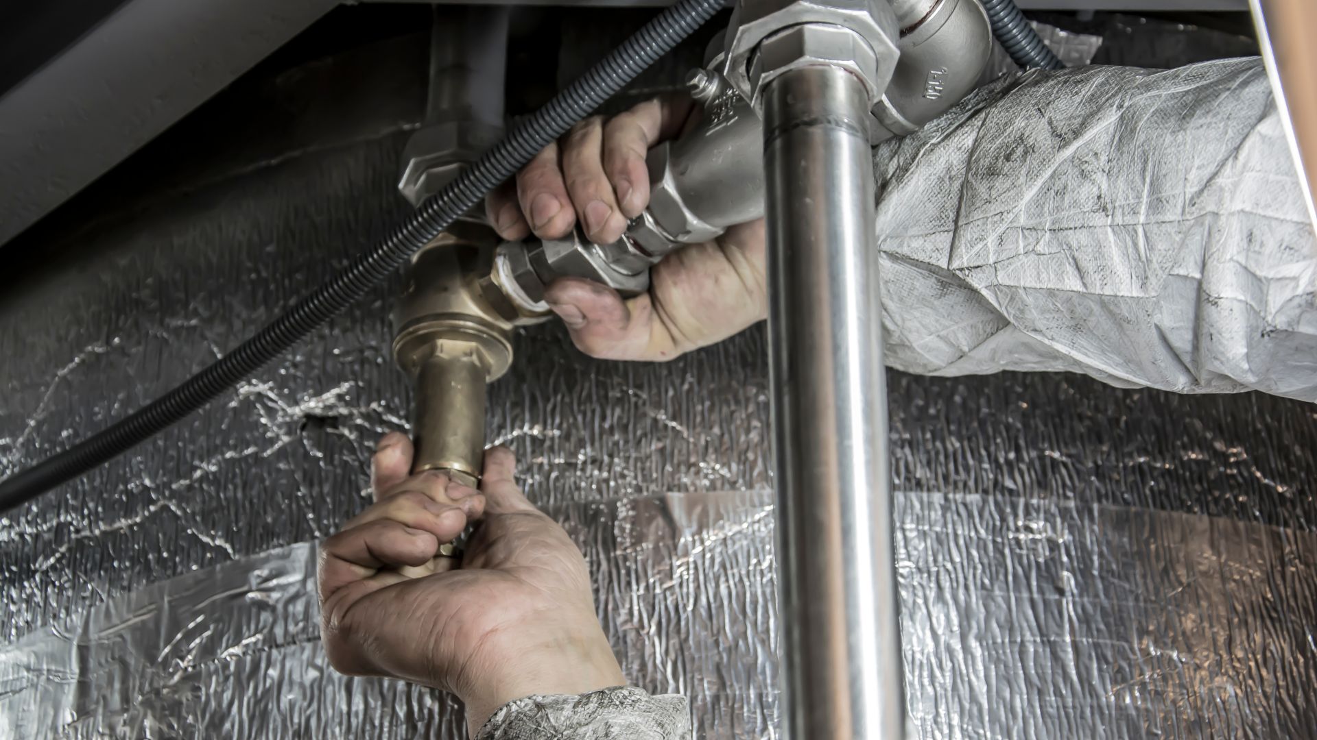 Hands tightening plumbing pipe connection with metallic wrench
