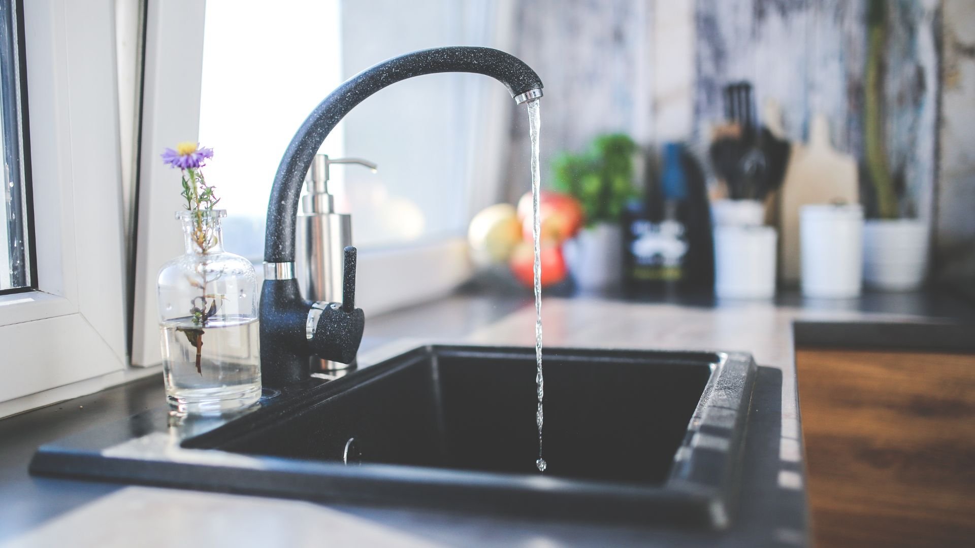 Black kitchen sink with running water and flower in glass vase