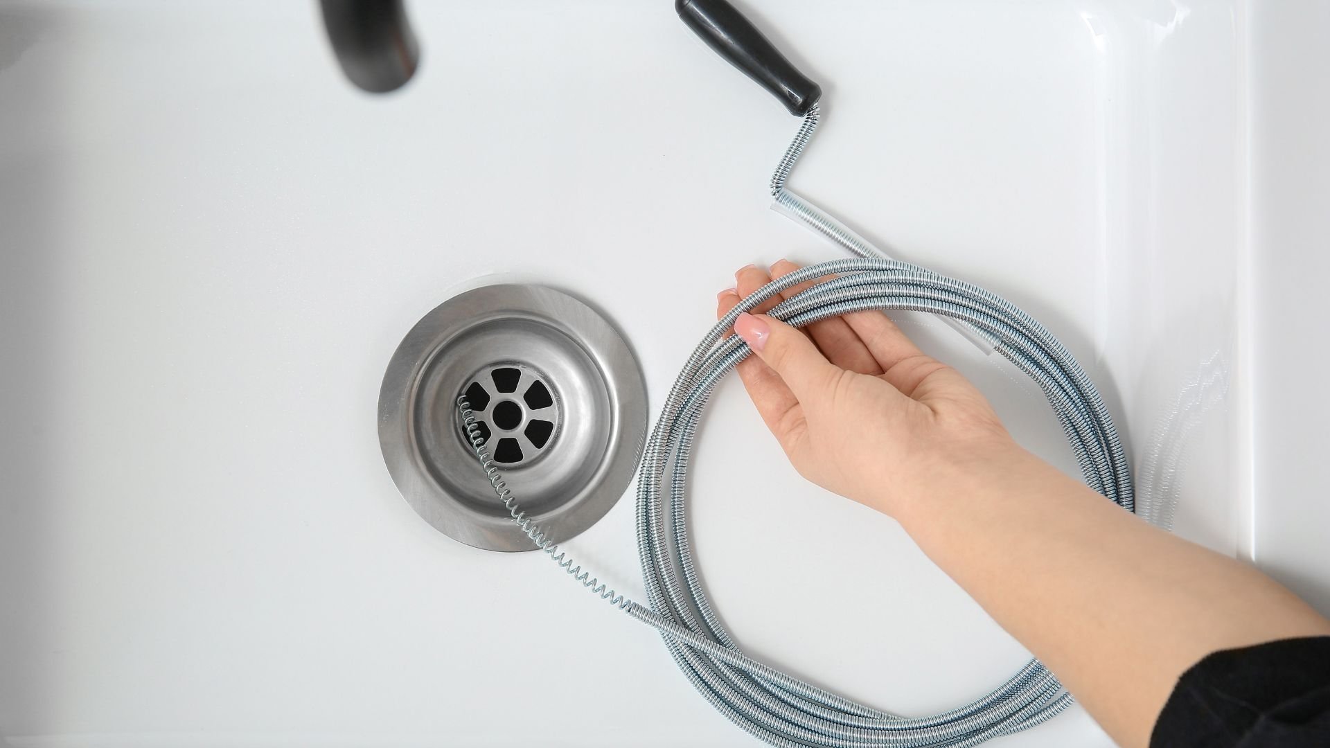 Hand holding drain snake next to sink drain for plumbing maintenance