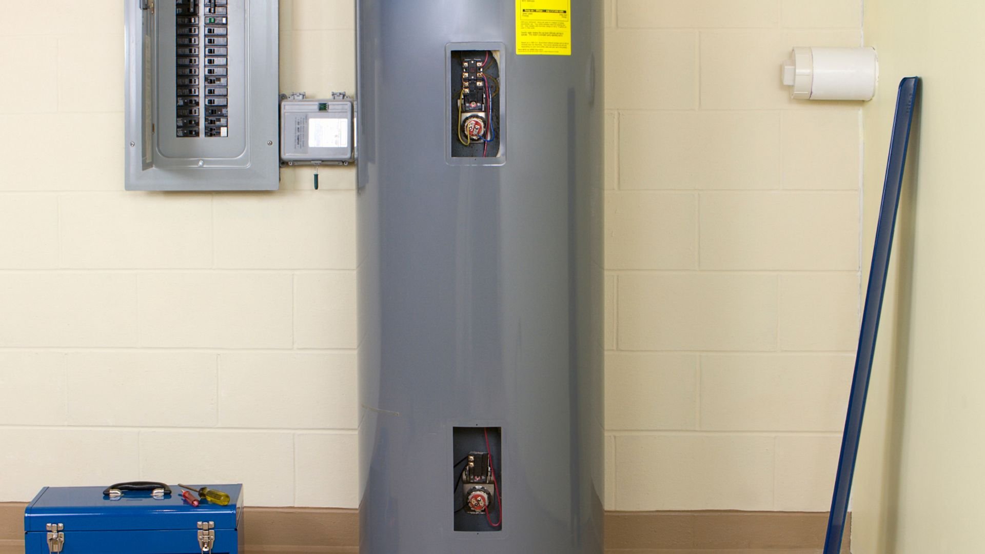 Gray water heater with electrical panel and blue toolbox in utility room
