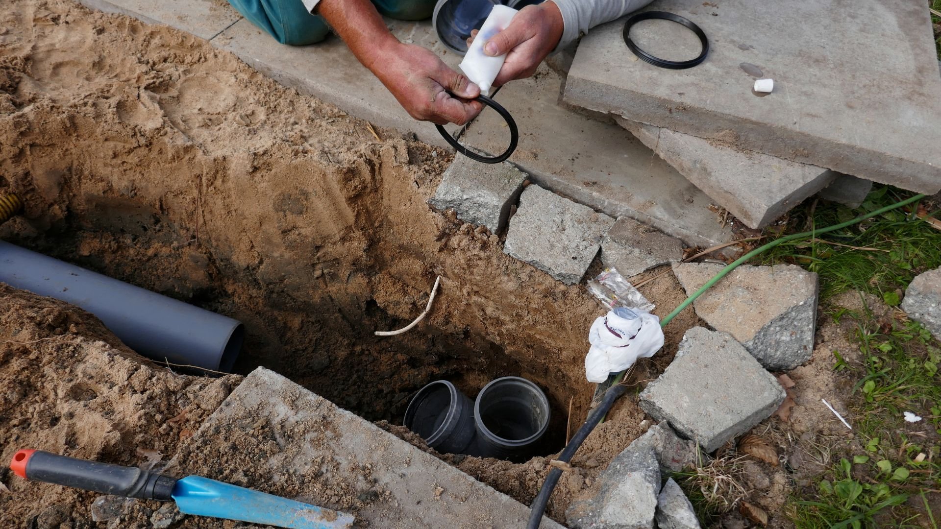 Plumbing repair with pipes and hands working in an excavated ground hole