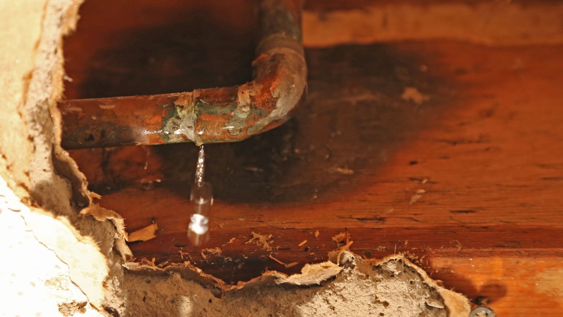 Rusty leaking pipe dripping water onto damaged wooden surface