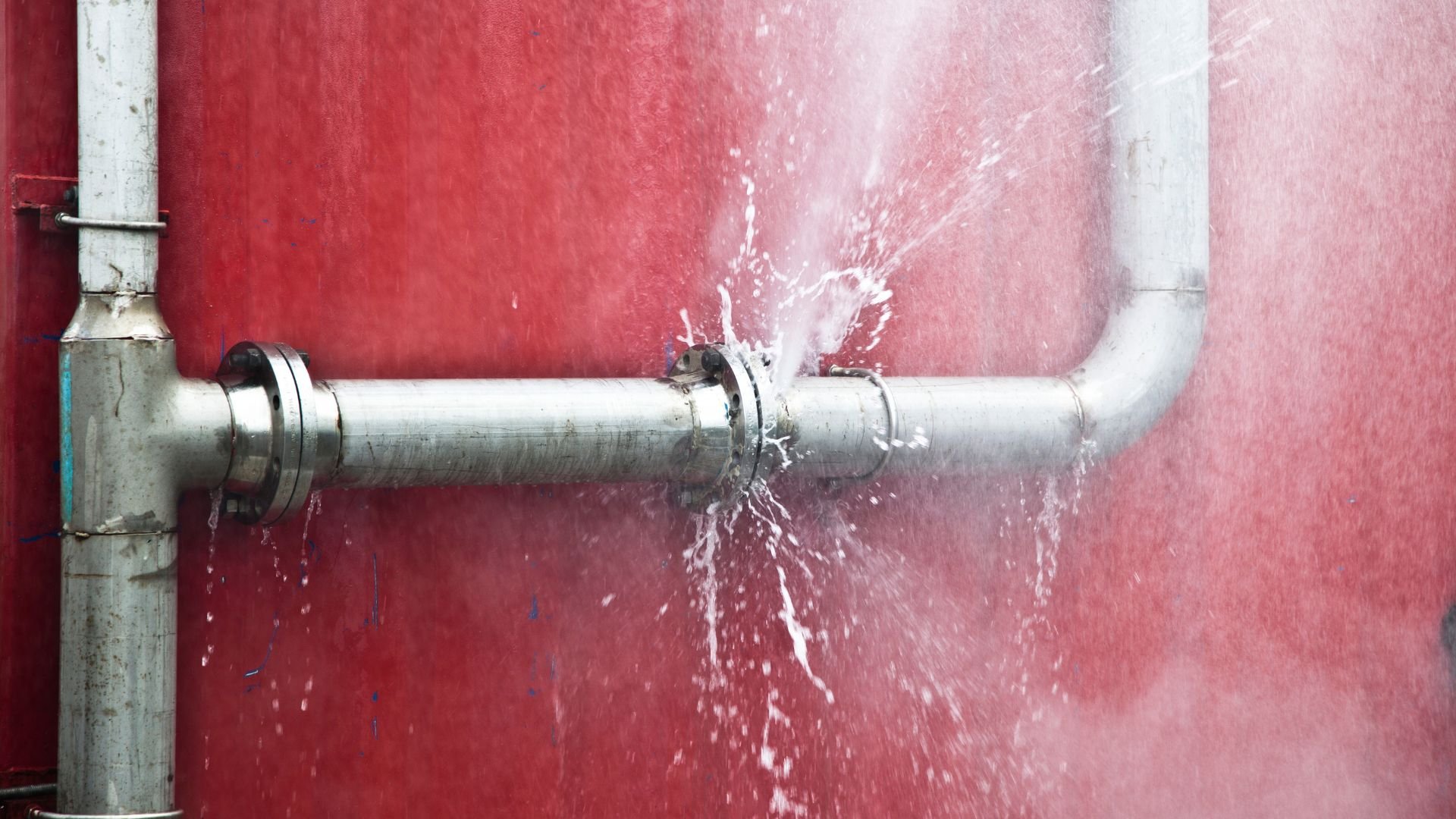 Leaking water pipe with spray against red and white background