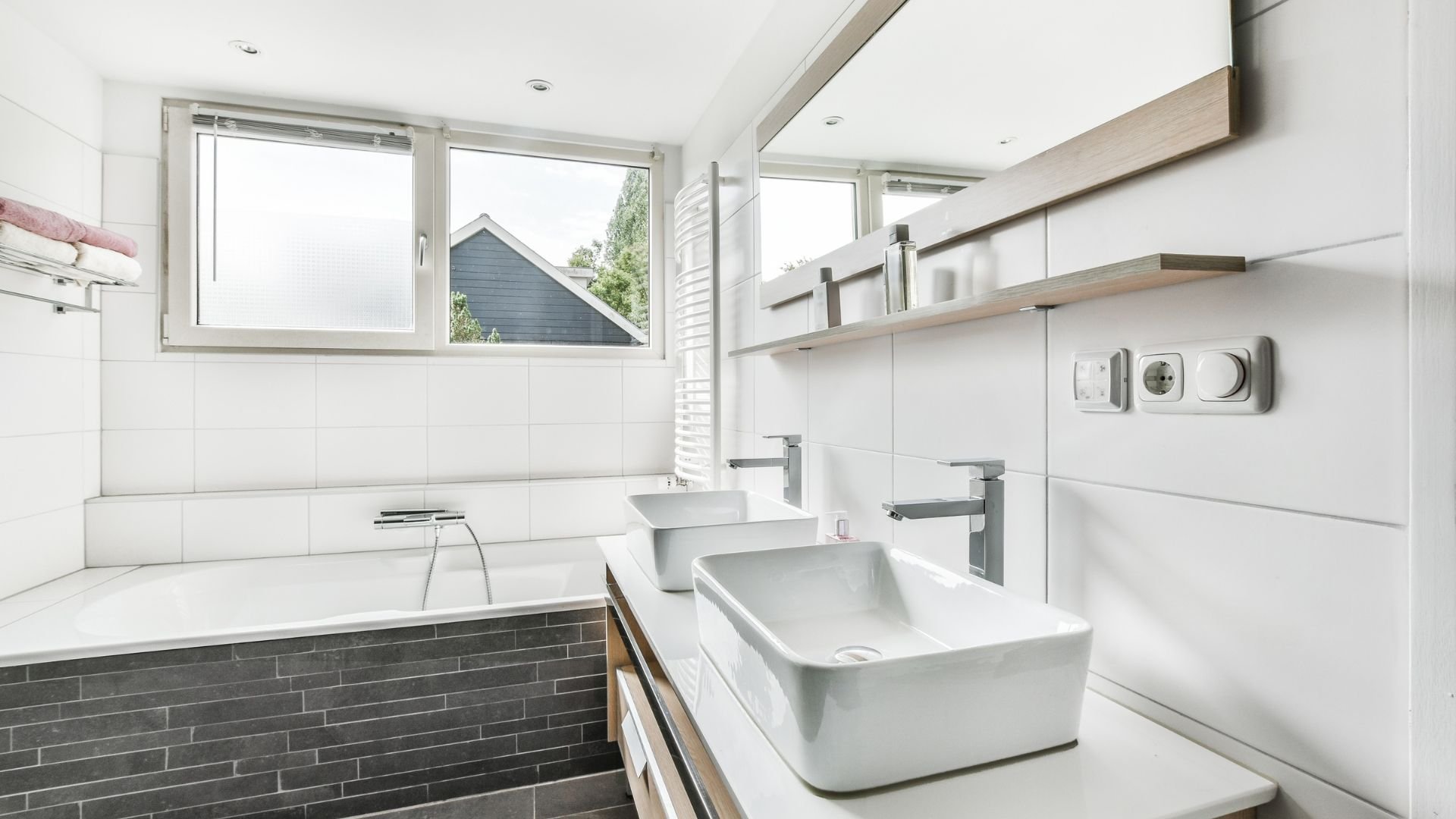 Modern white bathroom with bathtub, sink, and large windows