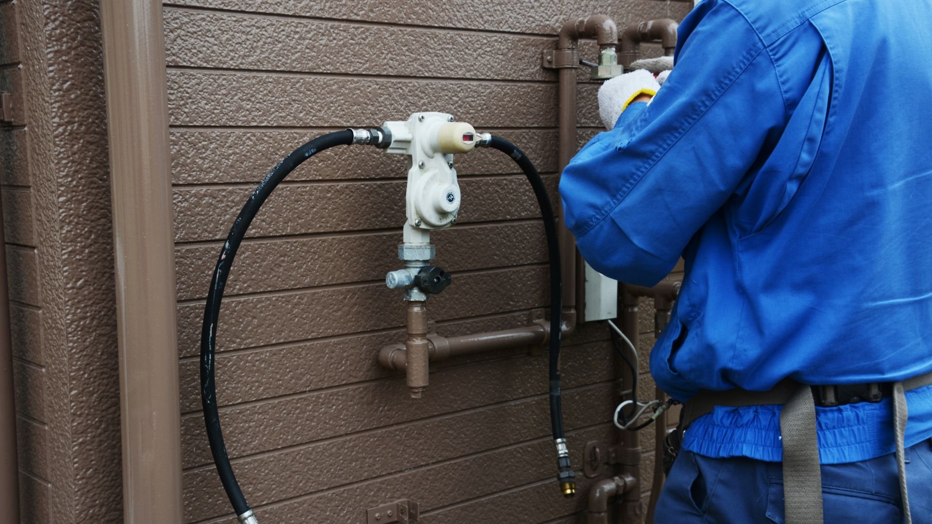 Technician in blue uniform checking water pipe connection on exterior wall