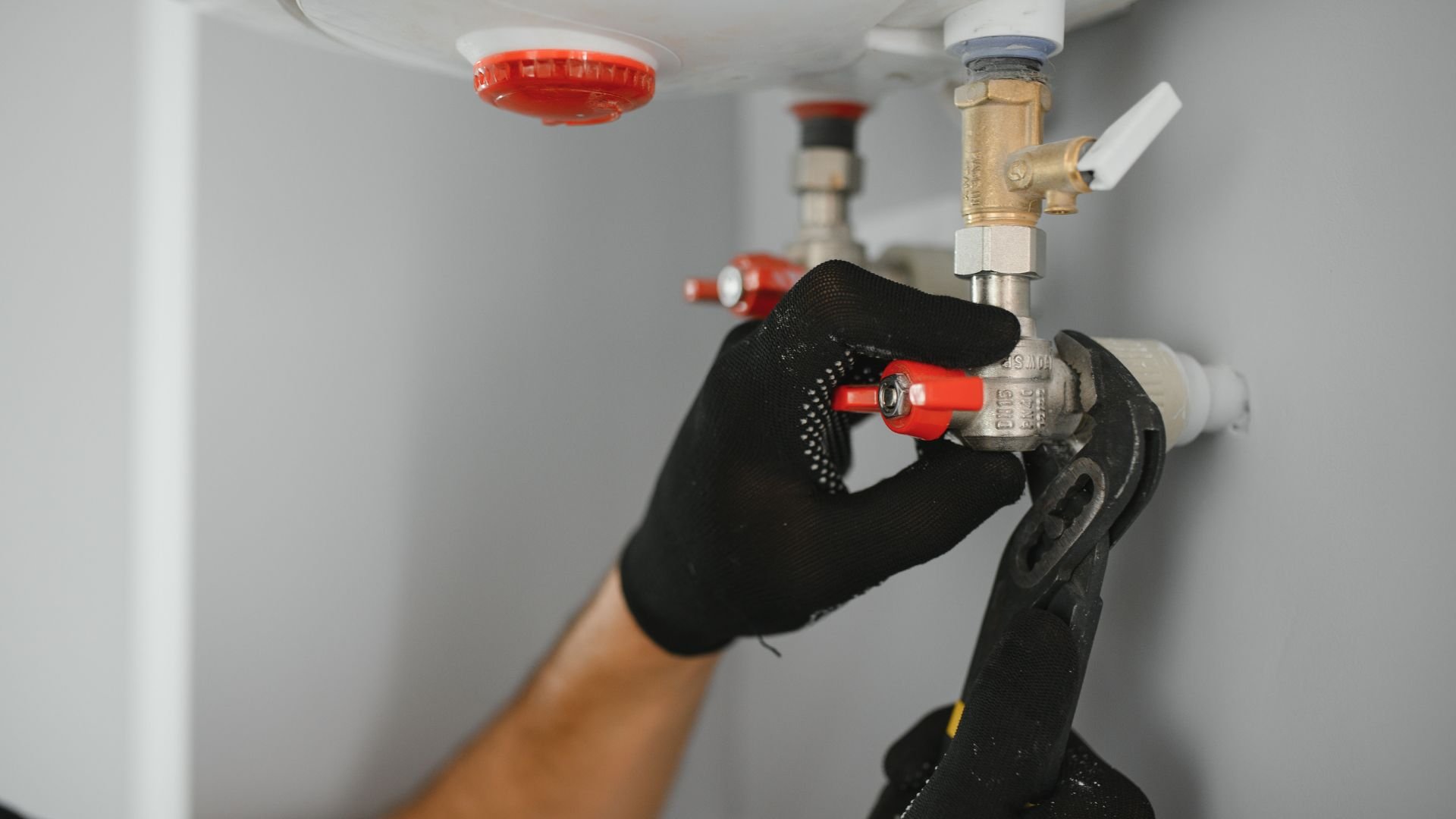 Gloved hand adjusting plumbing valve with wrench near water heater