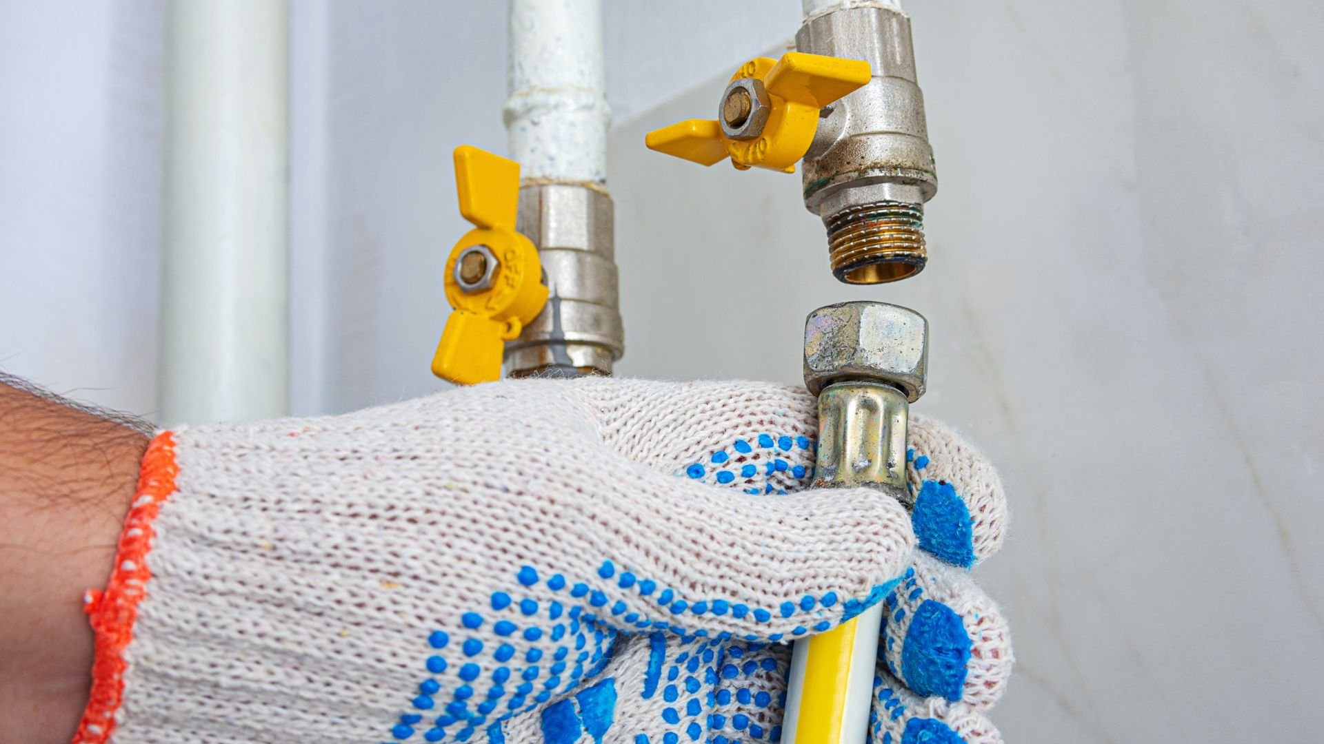 Hand in work glove adjusting yellow and metallic plumbing valves