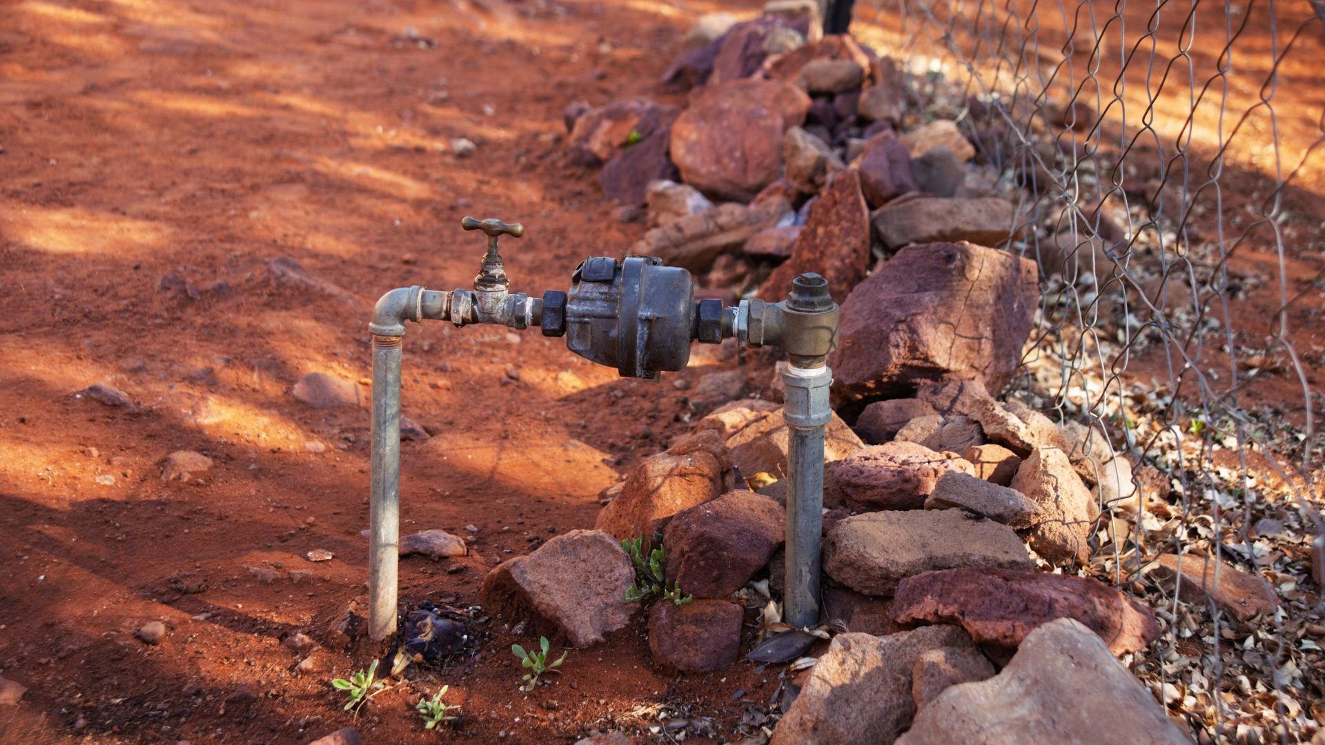Water pipe and valve amid rocky red soil with sparse vegetation