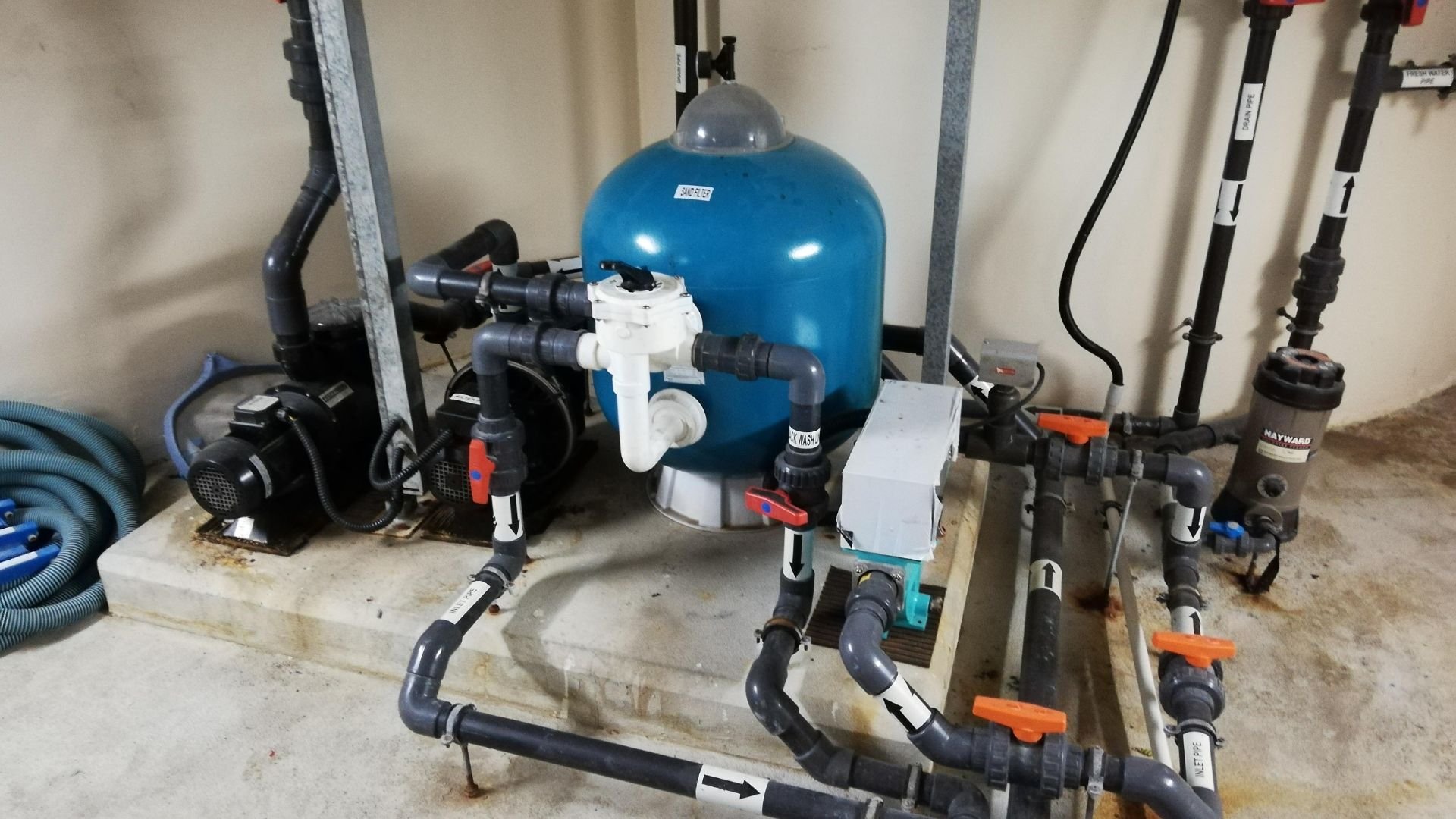 Pool filtration system with blue tank, pipes, and pumps in mechanical room