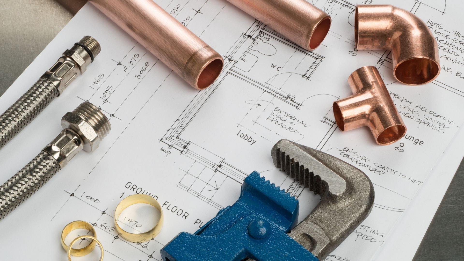 Plumbing tools and copper pipes on architectural blueprint